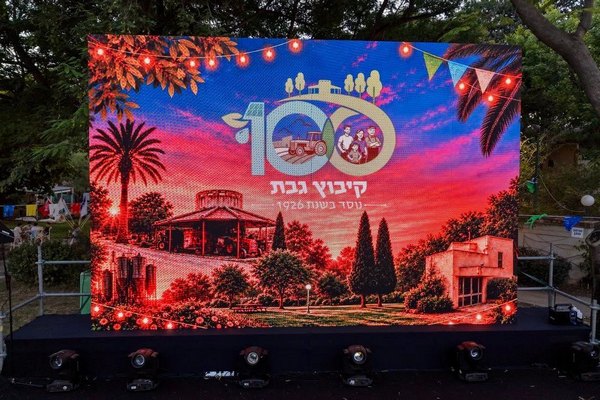 במה ועליה מסך המציג את סמל חגיגות המאה לקיבוץ גבת